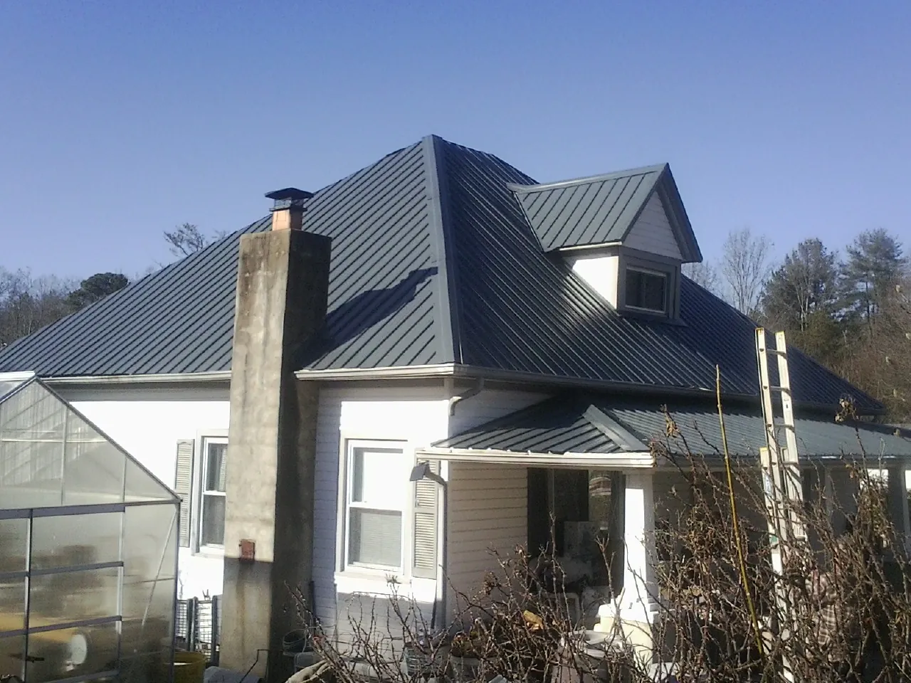 Dark blue standing seam metal roof on a white farmhouse with dormer — Slate & Tile Roof Repair by Roofing Brothers in Kremlin