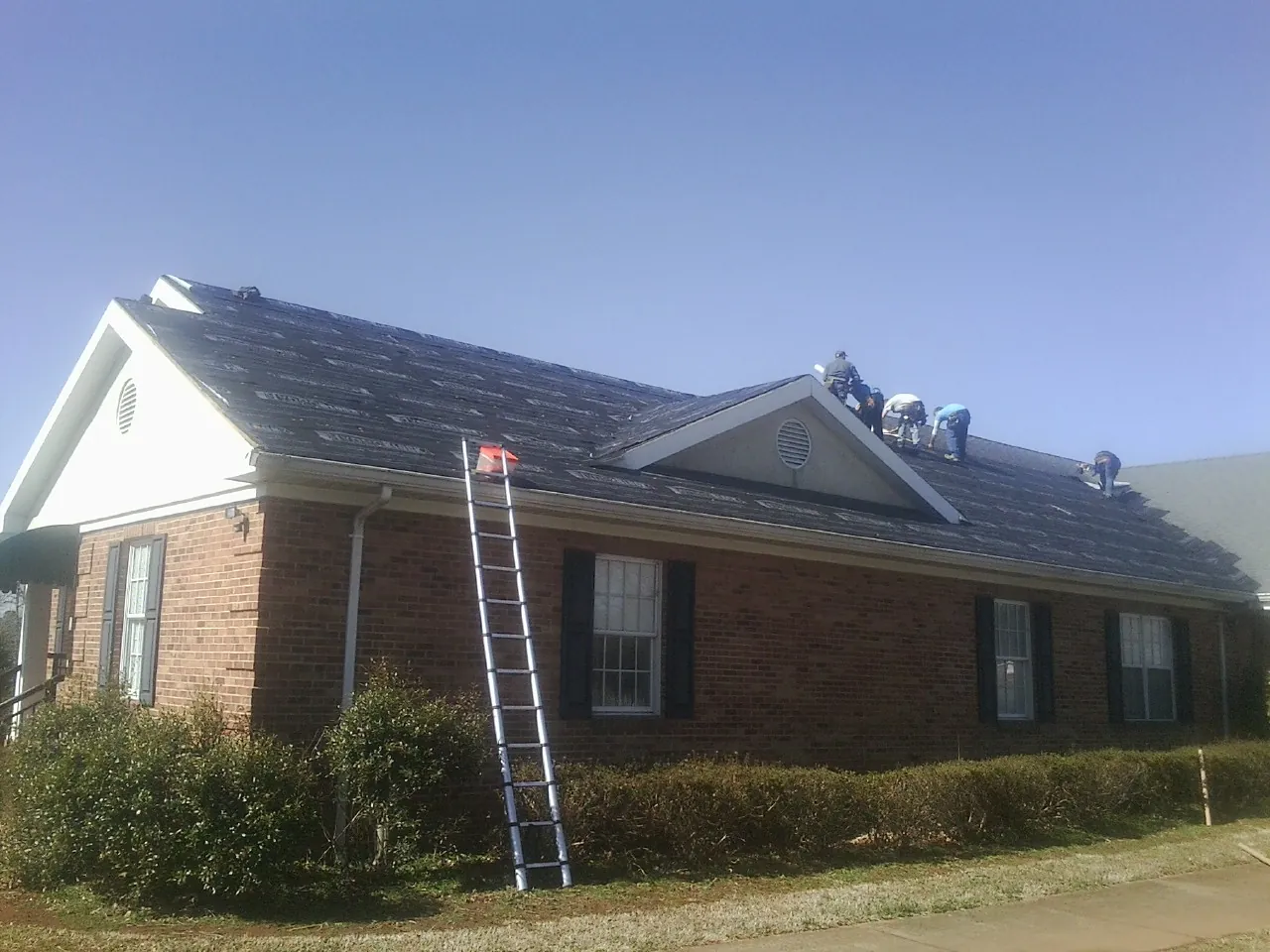 Crew tearing shingles off a brick ranch roof with a ladder set — Emergency Roof Repair work by our crew in Kremlin