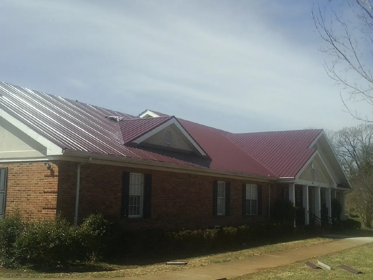 Red metal roof with gabled entries on a long brick building, from a Hail Damage Roof Repair job in Kremlin