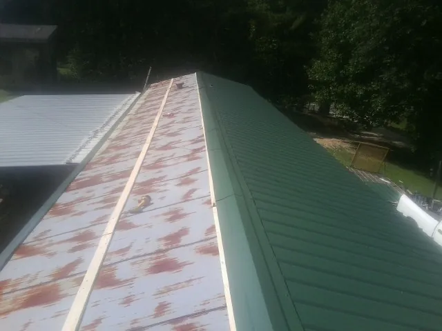 Old rusted panels beside newly installed green metal roofing — Wind Damage Roof Repair by Roofing Brothers in Kremlin