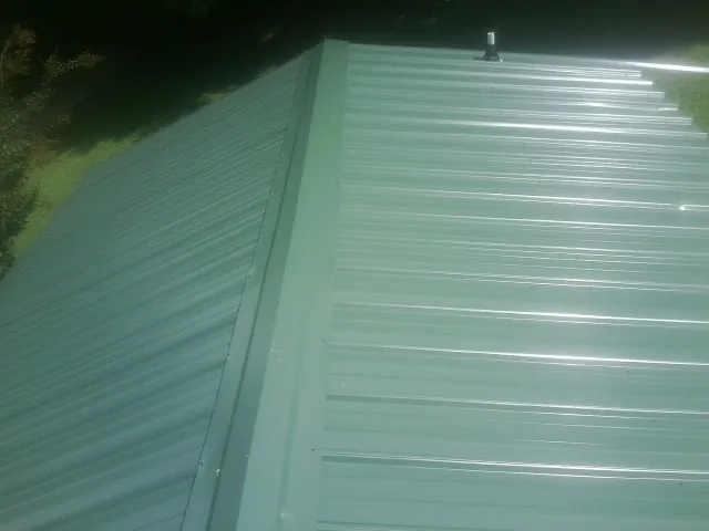 New green metal panels meeting at the ridge of a roof — Flat Roof Repair work by our crew in Kremlin