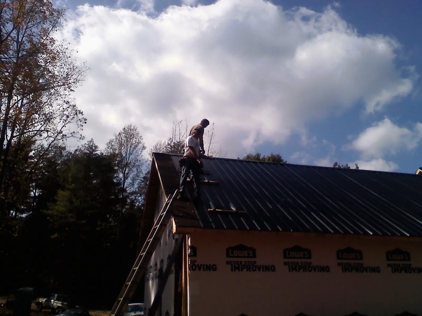 Roofer fastening dark metal panels high against a cloudy sky, from a Roof Inspection job in Kremlin